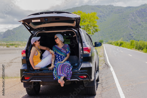 Two woman sitting at the car trunk on a road trip. © bignai