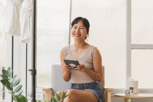 Portrait of young attractive cheerful Asian woman holding digital tablet looking at camera with smiley face. Happy smile freelance teenager using tablet with internet for the business