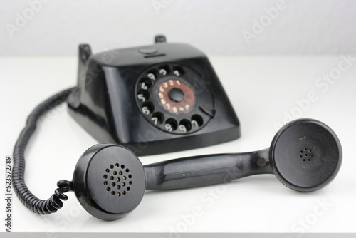 old antique dial operated telephone black out of bakelite on white background isolated side view front view with cable  reciever handset digits dial. Communication old fashioned classic