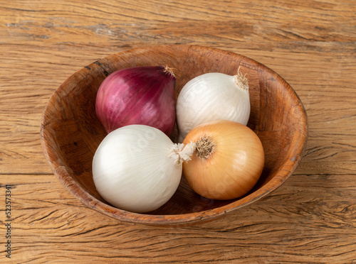 Assorted onions in a bowl over wooden table