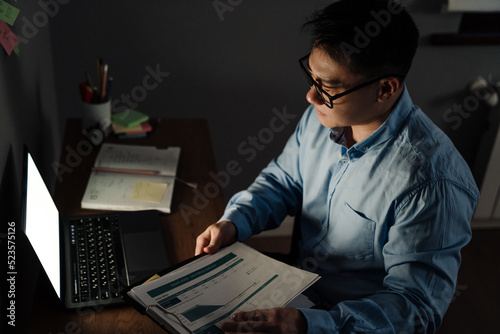Adult tense asian man with documents and laptop working