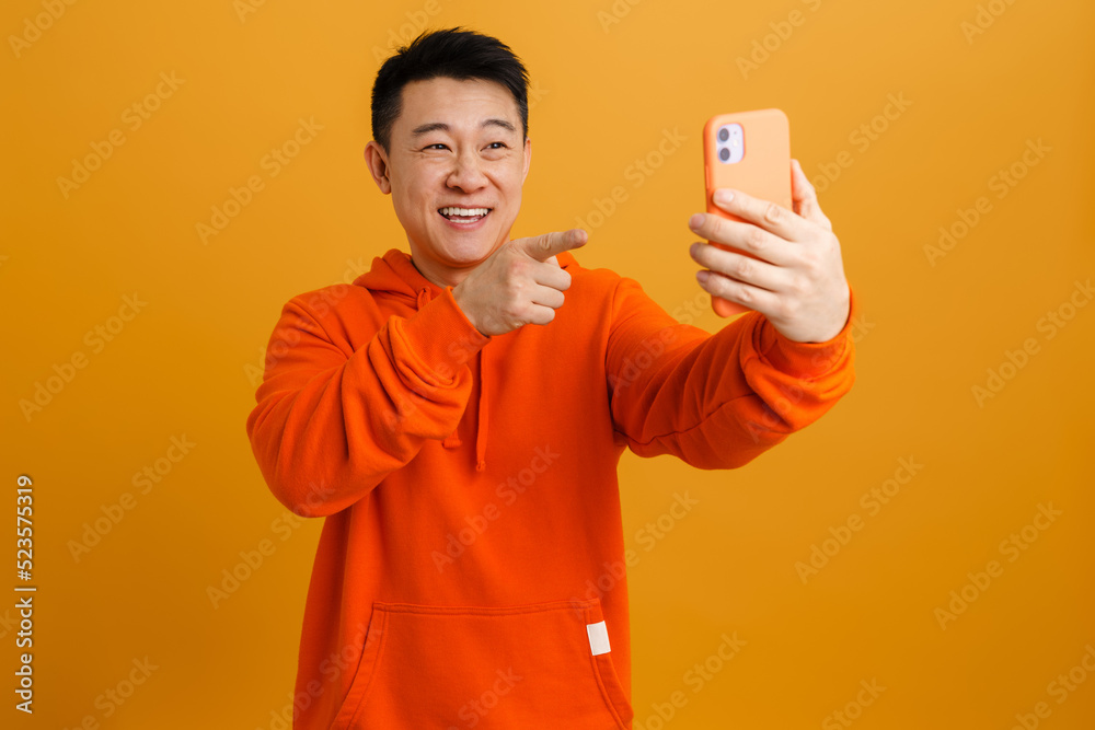 Happy brunette asian adult man rejoicing while using cellphone Happy brunette asian adult man rejoicing while using cellphone