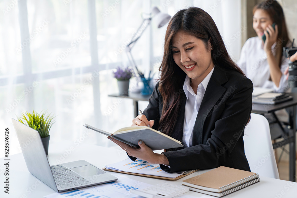 Asian businesswoman writing on paper and using laptop to searching data for working Asian businesswoman writing on paper and using laptop to searching data for working