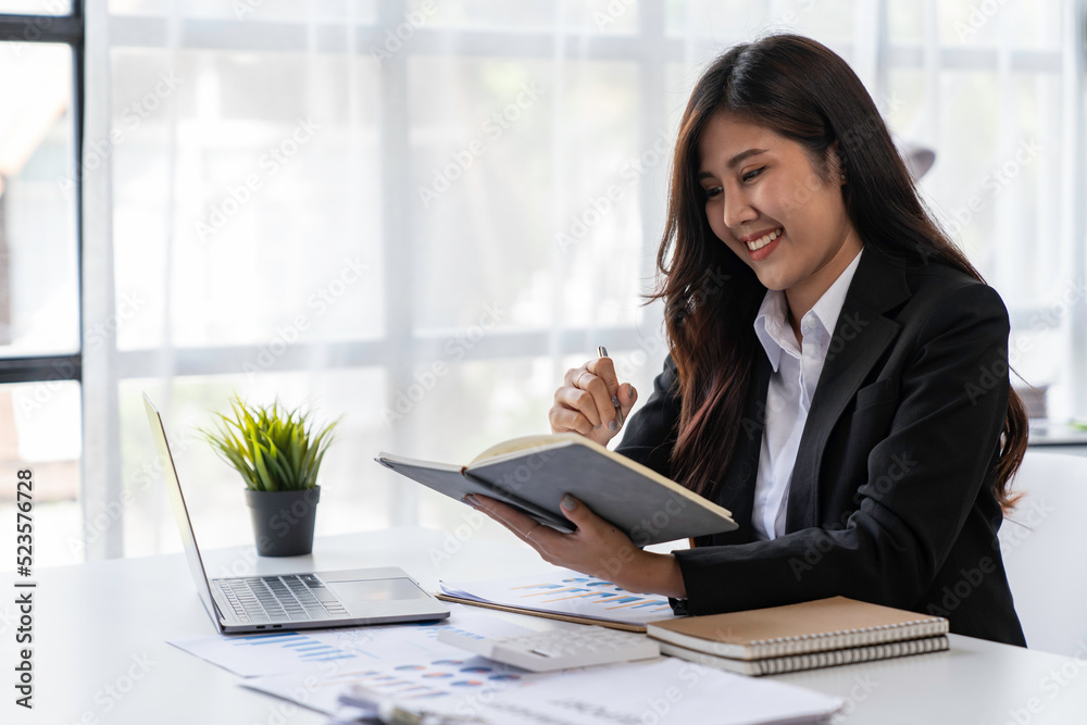 close up of Asian businesswoman writing on paper and using laptop to searching data for working close up of Asian businesswoman writing on paper and using laptop to searching data for working