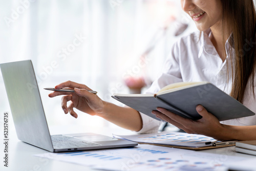 close up of Asian businesswoman writing on paper and using laptop to searching data for working © crizzystudio