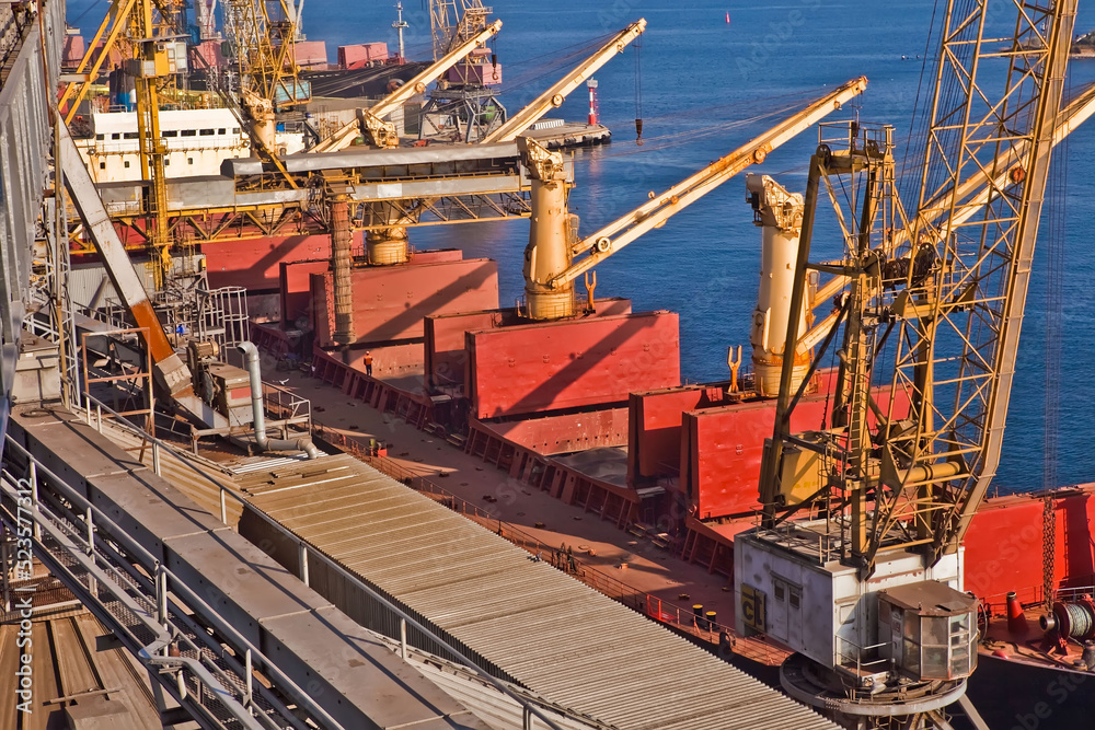 Loading grain into holds of sea cargo vessel in seaport from grain storage.