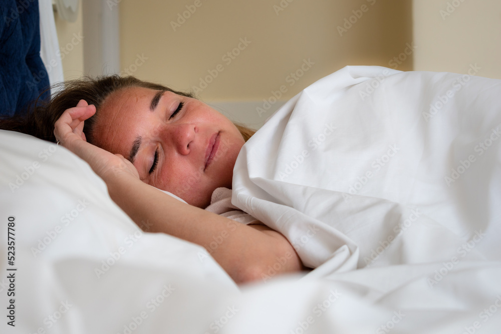 Mujer durmiendo tranquilamente en cama con sábanas y frazadas blancas