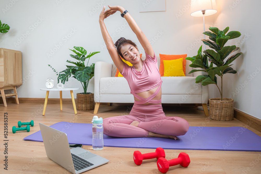 A young Asian woman doing her workout in her room and stretching for take a relaxation and cool down after the exercise for her own healthy