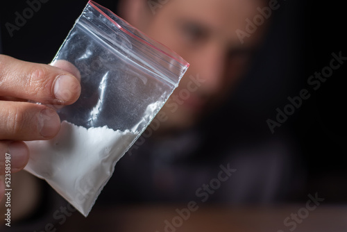 Concept drug addiction. Man hand holds plastic packet or bag with cocaine or another drugs