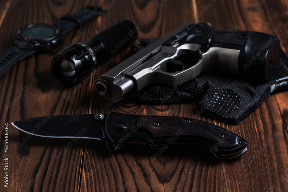 Obraz premium Folding pocket knife with pistol and flashlight on wooden background