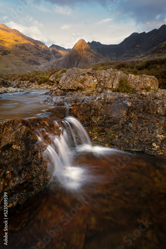 Small trickling waterfall with stunning view of Cuillin mountains dappled in golden light. Fairy Pools  Isle of Skye  Scotland  UK.