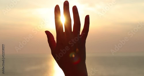 Female hand touching the sun, sunlight passing through fingers at sunset on the sea, slow motion closeup shining sun and the sea vacation, season travel nature idyllic