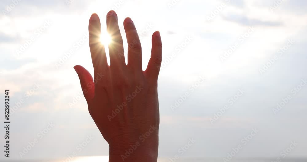 Female hand touching the sun, sunlight passing through fingers at sunset on the sea, slow motion closeup shining sun and the sea vacation, season travel nature idyllic Female hand touching the sun, sunlight passing through fingers at sunset on the sea, slow motion closeup shining sun and the sea vacation, season travel nature idyllic