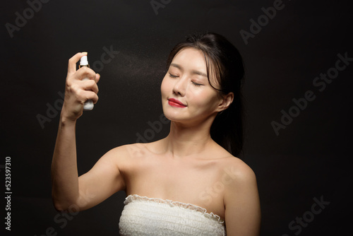 Beautiful woman applying spray water on face on neutral background
