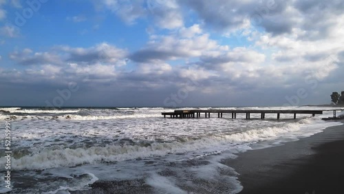 An impressive sea storm. Sea waves crash against coastal rocks, creating an explosion of water, and crash onto a sandy shore of black volcanic sand. Without people.