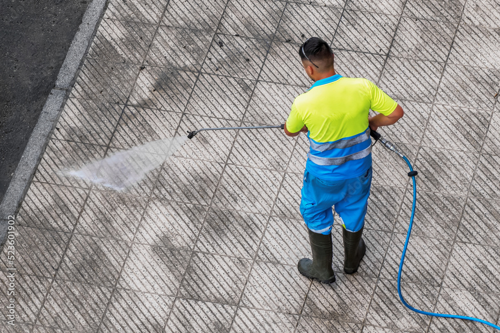 Street washer man washing dirty street pavement with high pressure water machine