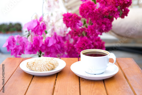 Cup of coffee and sesame cookie on the wooden table with bouquet of pink flowers