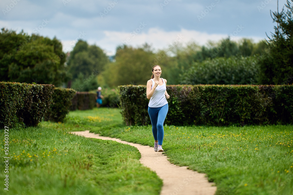 Woman in her 30s runs in public park in summer.