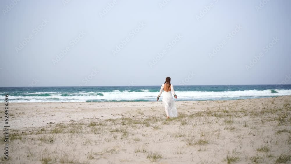 A woman walks along the beach. Slender female legs and feet walking on the sand on a sea water beach on a sandy beach. Beautiful woman in a white dress walks on the sea surf
