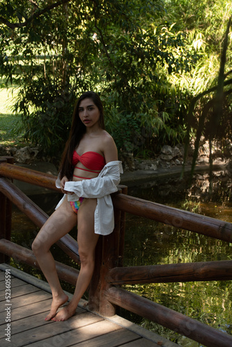 Venezuelan brunette girl with red bikini on a wooden bridge in a park.