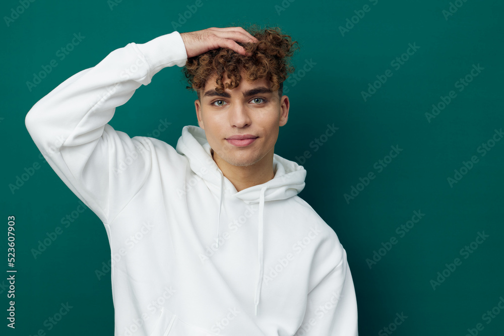 Fototapeta premium a handsome man stands on a green background in a white hoodie and poses relaxed with his hand behind his head. Horizontal Studio Photography