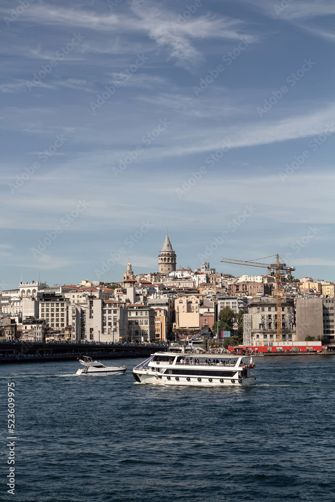 View of a tour boat and yacht on Golden Horn part of Bosphorus in Istanbul. Galata tower and Beyoglu district are in the view. It is a sunny summer day.