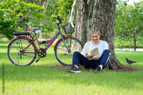 happy senior man resting and reading a book under the tree after ride a bicycle,elderly retired man relaxing among nature atmosphere,concept old people lifestyle,relaxing,resting,health care,wellbeing