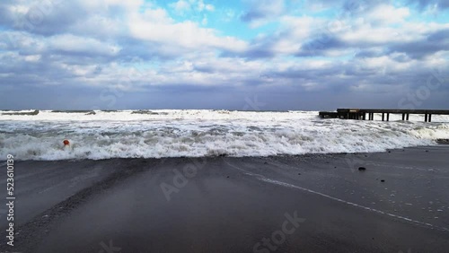 An impressive sea storm. Sea waves crash against coastal rocks, creating an explosion of water, and crash onto a sandy shore of black volcanic sand.