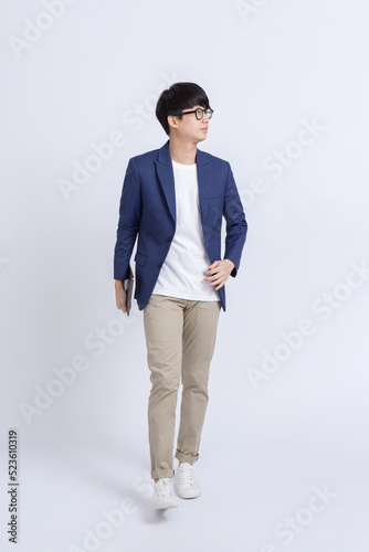 Confident young business man in eyeglasses with digital tablet walking and looking aside on white background