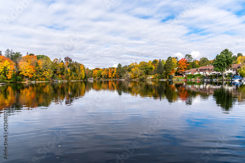 Houses and boathouses along the forested shores of a lake on a cloudy autumn morning. Fall foliage and reflection in water.