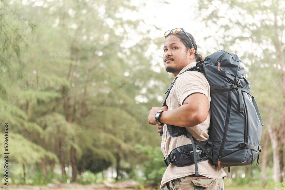 Backpacker Travel Concept , Portrait of an Asian man with a large bag on his back in the forest, looking at the camera.