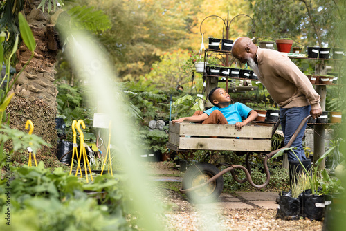 Happy senior african american man with his grandson using barrow in garden