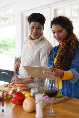 Happy biracial couple preparing food using recipe on tablet in kitchen