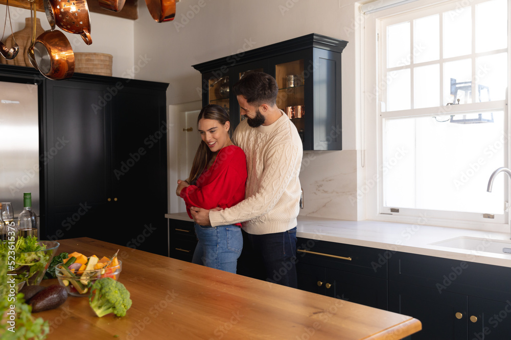 Obraz premium Happy caucasian couple smiling and embracing in kitchen
