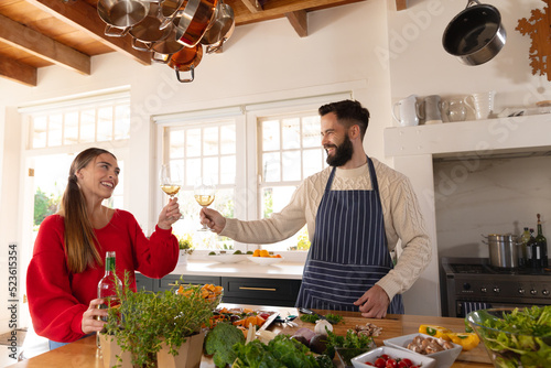 Happy caucasian couple preparing food in kitchen, making a toast with glasses of white wine