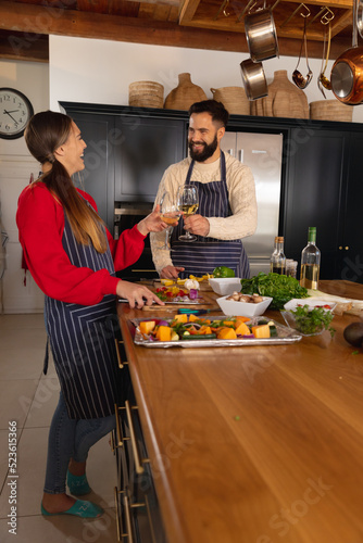 Happy caucasian couple preparing food in kitchen, making a toast with glasses of white wine