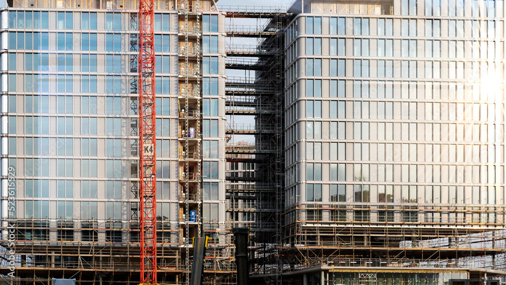 the sun's rays are reflected in the glass facade of a multi-storey building under construction