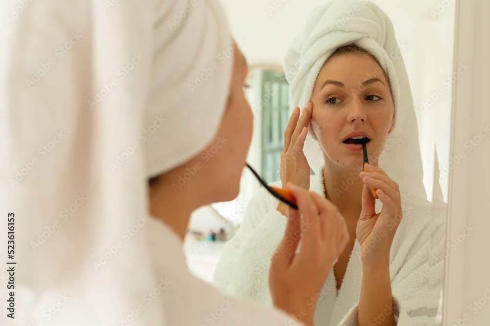 Happy caucasian woman wearing robe, brushing teeth and looking at mirror in bathroom Happy caucasian woman wearing robe, brushing teeth and looking at mirror in bathroom