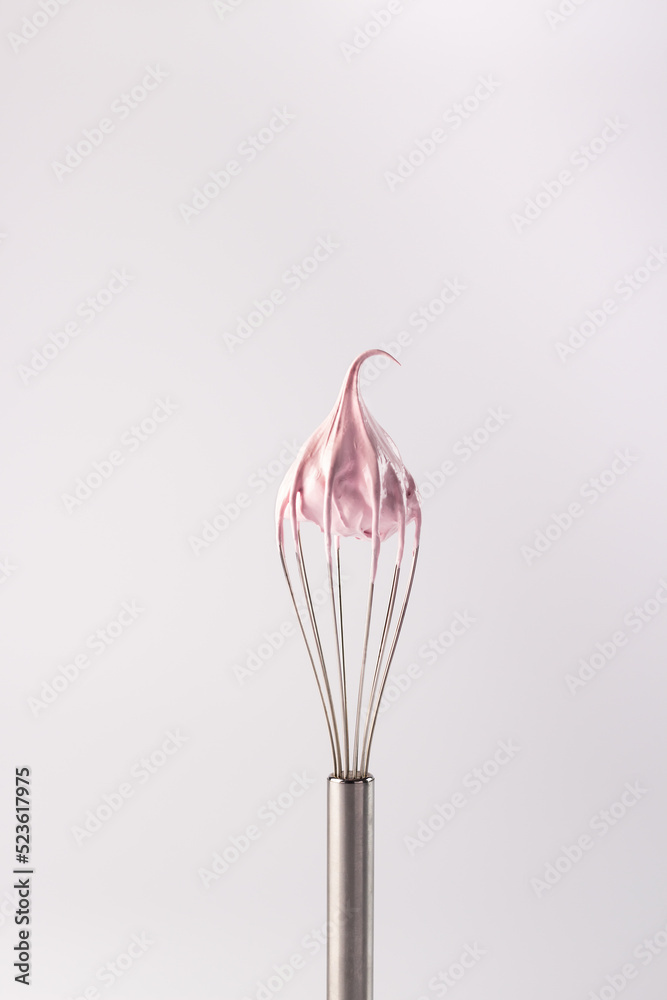 Whisk with cream on a white background. Pink whipped cream made from protein and sugar on a whisk. Marshmallow or raspberry meringue. Whisk with cream on a white background. Pink whipped cream made from protein and sugar on a whisk. Marshmallow or raspberry meringue.