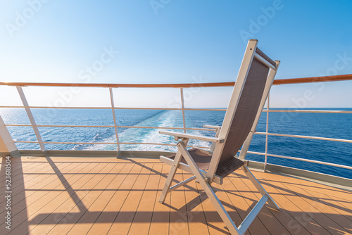 Vue d'une chaise longue sur le pont d'un navire de croisière dans le sillage d'un navire de croisière. Vue depuis la poupe du navire.	 photo
