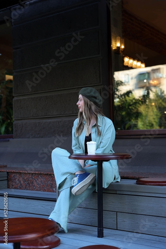 a girl sits in a hat in a cafe on the street, waiting for an interlocutor
