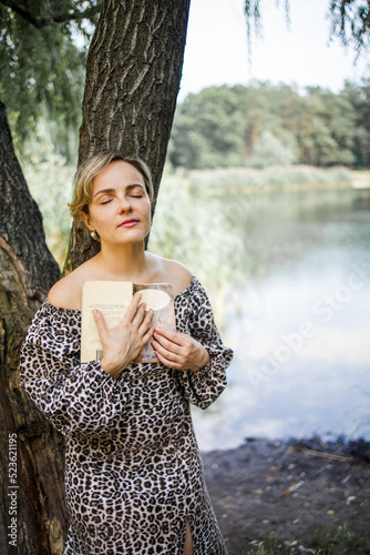 Beautiful middle aged woman stanging near a single big tree in green field. photo