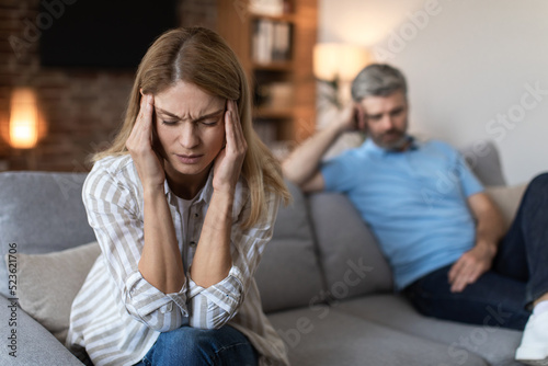 Upset offended mature european husband ignores wife, lady suffers from headache in living room interior