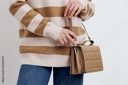 a close horizontal photo of a beautiful, stylish beige women's bag worn over the shoulder on a girl in a striped sweater