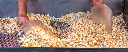 Salting and mixing freshly popped kettle corn. Operator mixes it with salt and perhaps sugar allowing unpopped waste kernels to fall through the holes in the sifting tray. photo