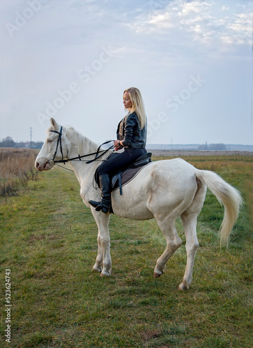 young beautiful blond smiling woman with long hair riding a white horse with blue eyes in autumn field 