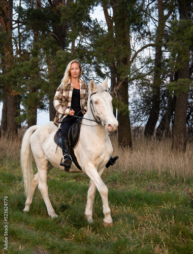 young beautiful blond smiling woman with long hair  riding a white horse with blue eyes in autumn field  © Tetatet