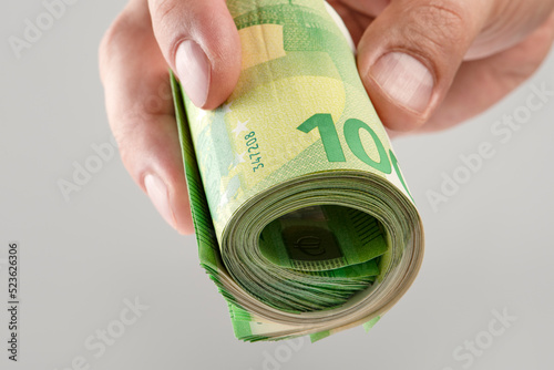 The hand holds a roll of 100 euro banknotes. Euro banknotes rolled up in a white man's hand on a gray background. The concept of financial assistance, real estate purchase, loan or insurance payment.