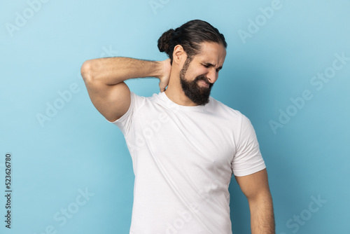 Canvas Print Portrait of man with beard wearing white T-shirt touching neck, feeling acute pain, suffering spine problems, osteochondrosis, frowning face