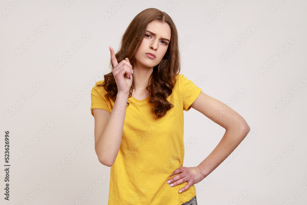 You better do what I say! Portrait of young female wearing yellow casual T-shirt looking at camera with serious face and shows finger warning gesture. Indoor studio shot isolated on gray background. You better do what I say! Portrait of young female wearing yellow casual T-shirt looking at camera with serious face and shows finger warning gesture. Indoor studio shot isolated on gray background.
